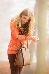 秋时流行的女尚孩穿着鲜活服装手拿着棕色皮包手提袋在秋雾公园户外行走图片