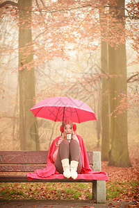 女孩坐在公园里女士拿着伞子从杯上喝咖啡坐在长椅上女孩坐在公园里拿着伞子坐在公园里图片
