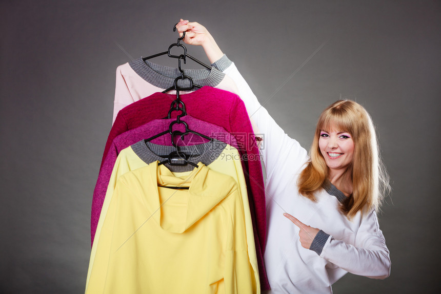 零售和销金发美女时装服顾客与衣着多彩灰色背景的手指衣架对着顾客