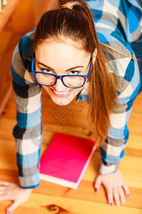 学校教育概念女生时髦穿着蓝眼镜在地板上做马尾辫背书阅读图片
