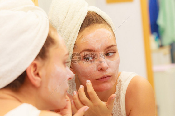 妇女用面罩湿润的皮肤霜在脸部看卫生间镜子时使用女孩要照顾她的皮肤层润湿剂皮肤科疗养妇女要在浴室里用面罩霜图片