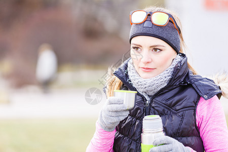 女旅行者在寒冷的天气中穿着温暖运动服装在户外穿着温暖运动服装的女旅行者在寒冷的天气中喝着从真空瓶子热水中取出的茶暖和起来图片