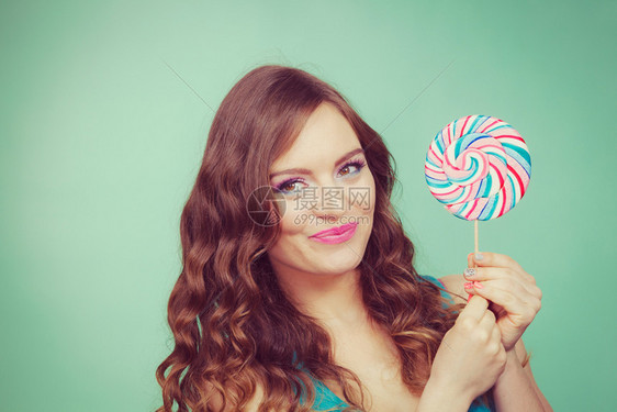 迷人的有魅力女孩拿着多彩的棒糖甜美食物和享受概念工作室拍摄的绿色蓝背景刻画的图像图片