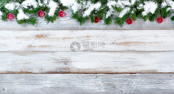 雪的顶端边界覆盖了圣诞常青树枝和白旧木上的红蜡烛图片