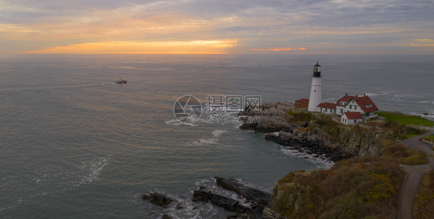 一艘渔船在日出时伊丽莎白角波特兰正灯附近沿着海岸航行图片