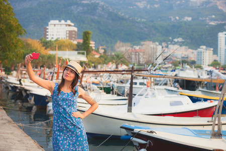 戴帽子的年轻女旅行者在夏季阳光明媚的地中海城市拍摄自带智能手机相的年轻女旅行者在暑假时拍摄自带智能手机相的年轻女旅行者在夏季拍摄图片