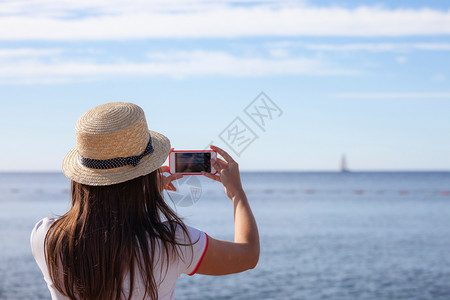 戴帽子的年轻女旅行者用智能手机照相拍摄夏季阳光明媚的海景照片Brunette女孩在暑假拍摄照片黑山布德瓦戴着帽子的年轻女旅行者用图片