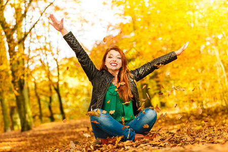 红发长女人在秋天的公园里向空中扔叶子图片