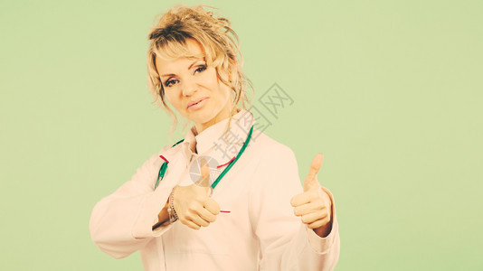 女医生露出拇指穿白色专业制服颈部有听诊器的妇女中年成功的药剂师护士穿绿色女医生露出拇指图片
