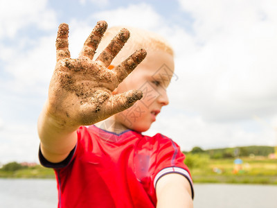 金发小男孩举着肮脏的泥巴手图片