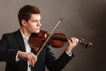 音乐激情爱好概念青年男子穿着优雅的木小提琴演奏工作室在黑暗背景中拍摄男子穿着优雅的小提琴演奏图片