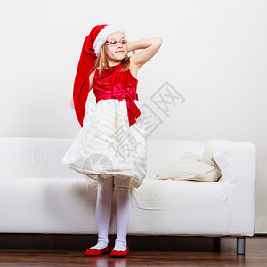 戴圣诞帽子的托德勒女孩穿着圣诞帽子和礼服的托德勒女孩站在沙发旁边图片