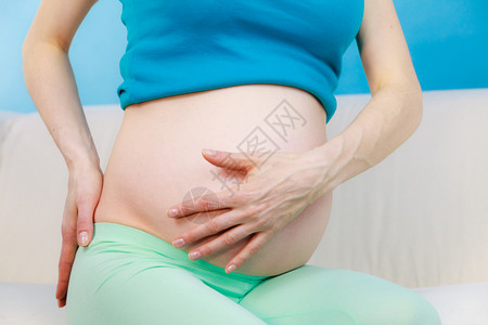 坐在沙发上手放背着手坐在沙发上的孕妇背部按摩疼痛怀孕和健康概念坐在沙发上她的背手放在她的背上图片