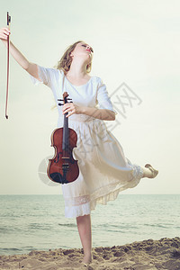 音乐爱好和日常激情概念海边滩上的妇女拿着小提琴跳海边的妇女拿着小提琴图片