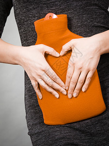 女腹痛将热红水瓶放在腹部作为治疗疼痛的药方用双手塑造心脏形状卫生保健女孩将热水瓶放在腹部用手塑造心脏形状图片