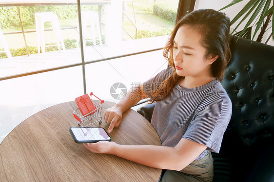 带有智能手机的小型妇女购物车用于互联网在线购物概念图片