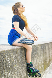 身穿溜冰鞋的年轻女子坐在海边休息图片