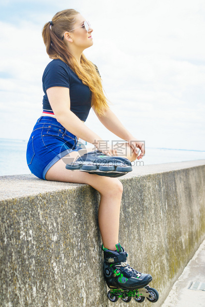 身穿溜冰鞋的年轻女子坐在海边休息图片