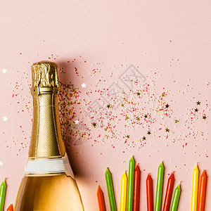 纯净的庆典香槟瓶子加冰淇淋喷洒金星以及粉红色背景的生日蜡烛顶端的景色粉红背的香槟瓶子加粉红色背景的喷洒图片