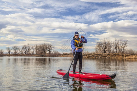 高官在科罗拉多州秋天或冬季的湖边划着一个可充气的站台爬上桨板图片