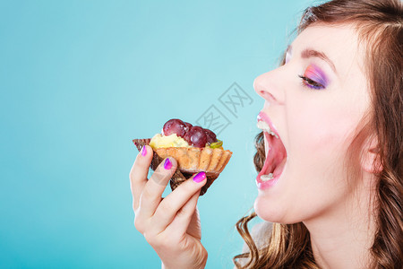甜美的食物饱和脂肪的概念妇女面对张开的嘴吃蛋糕蓝背景图片