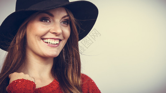 穿着红毛衣黑时装帽在工作室微笑和装扮带着棕色头发和黑帽子微笑的漂亮女孩图片