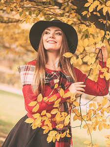 公园的秋季颜色概念女人站在树边穿着黑帽子和红色天候的迷人女士和非常时髦的围巾女人站在树边图片