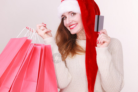 身戴圣达克萨斯帽子持有红色购物袋和信用卡购买礼品戴圣诞帽的妇女持有信用卡和购物袋图片