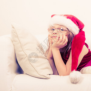女孩在圣诞节时的家庭间可爱的小女人爬在沙发上小女人躺在沙发上休息时间穿着红色的圣达克萨斯帽子和鞋可爱的小女人爬在沙发上背景图片