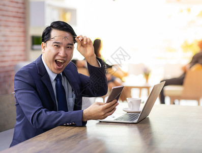 Businessman肖像以智能手机和平板电脑庆祝他在咖啡馆的成功图片