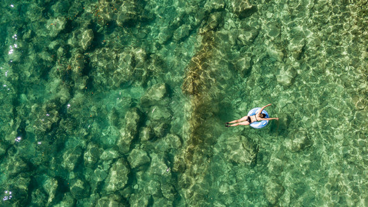 黄褐色的年轻女子在绿海中可充气的大圆圈中游泳空景象闪发光的女士在泰国度假时放松的空中景象Phuket黄褐色的年轻女子在绿海中可充图片