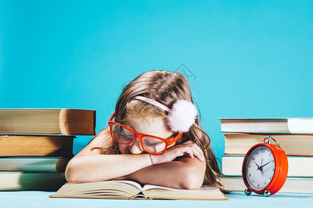 小女孩睡在一本公开的书上穿着有趣的红色眼镜旁边有一堆书回到学校图片