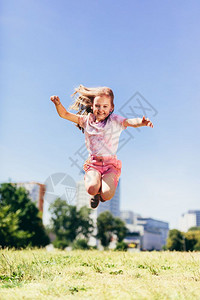 女孩穿着多彩的脏衣服在市公园跳高童年的乐趣在外面玩耍小女孩穿着多彩的脏衣服跳高在市公园图片
