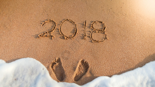 在湿沙滩上写下两个足迹和2018年数字的近距离图像冬季假日庆祝和旅行的概念在湿沙滩上写下两个足迹和2018年数字的近距离照片图片