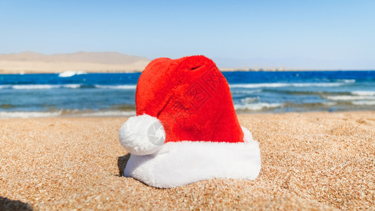 圣诞老人的帽子躺在沙滩上圣诞新年和冬季假期的旅行和游概念红圣诞老人的帽子躺在海滩上的沙图片