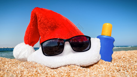 太阳镜红色Santa沙滩上的帽子和防晒霜圣诞节新年和冬季假日的旅行和游概念沙滩上的帽子和防晒霜近照圣诞节新年和冬季假日的旅行和游图片