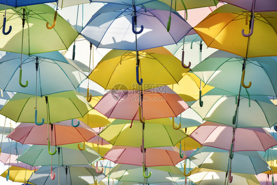 挂在有清蓝天空的步行道上装饰多彩雨伞图片