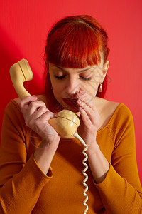 美貌女通过用旧电话覆盖接收器用扭曲的电线对着明亮红门用旧电话覆盖接收器从而流传言图片