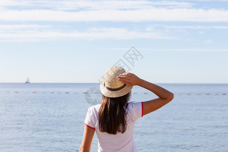 美丽的女孩看着海戴帽子的年轻女孩看着平静的海面图片