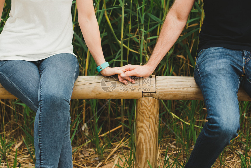 情侣在木栅栏上坐着牵手