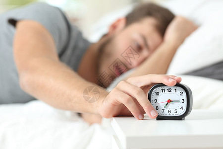 早上躺在床的疲倦男人关掉闹钟图片