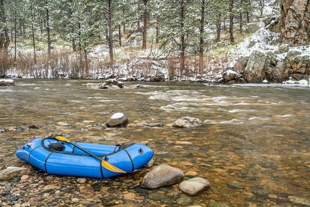 在春季暴风雪中在山河岸的上搭有桨可充气背包用于探险或冒赛的单人轻型木筏科罗拉多的Poudre河图片