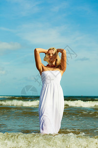 穿着长白色浪漫服装的迷人金发女子在夏天海中漫步图片