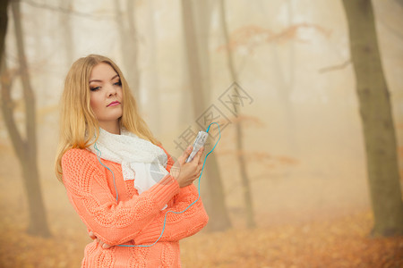 有耳机和智能听觉音乐的年轻女子雾中的孩秋天公园有耳机的妇女在公园听音乐图片