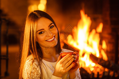 快乐的女子在壁炉里喝咖啡着的快乐女子在壁炉里喝着咖啡图片