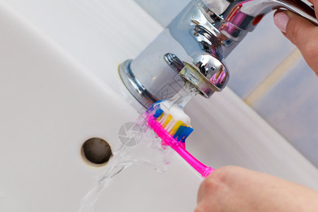 妇女手持牙刷和膏在洗手间水槽和背景龙头中手持牙刷在洗间图片