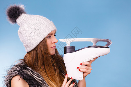 冬季体育活动概念身着温暖帽子和毛皮外衣的女孩拿着看滑冰蓝背景工作室拍摄的镜头身着冬帽的妇女看滑冰图片