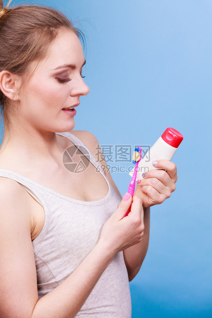 持牙刷和膏洗的妇女带着刷笑的姑娘快乐口腔卫生工作室拍蓝色背景图片
