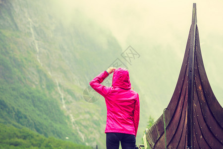 在挪威自然界的旧木型维京船附近站立的女旅游者看着迷雾山雨日旅游和概念在挪威自然界的旧木型维京船附近站立的旅游者图片