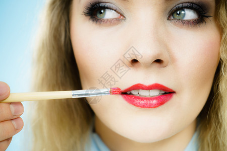 专业化妆艺术家在女时装模特嘴唇上应用红色印或刷子涂口红图片
